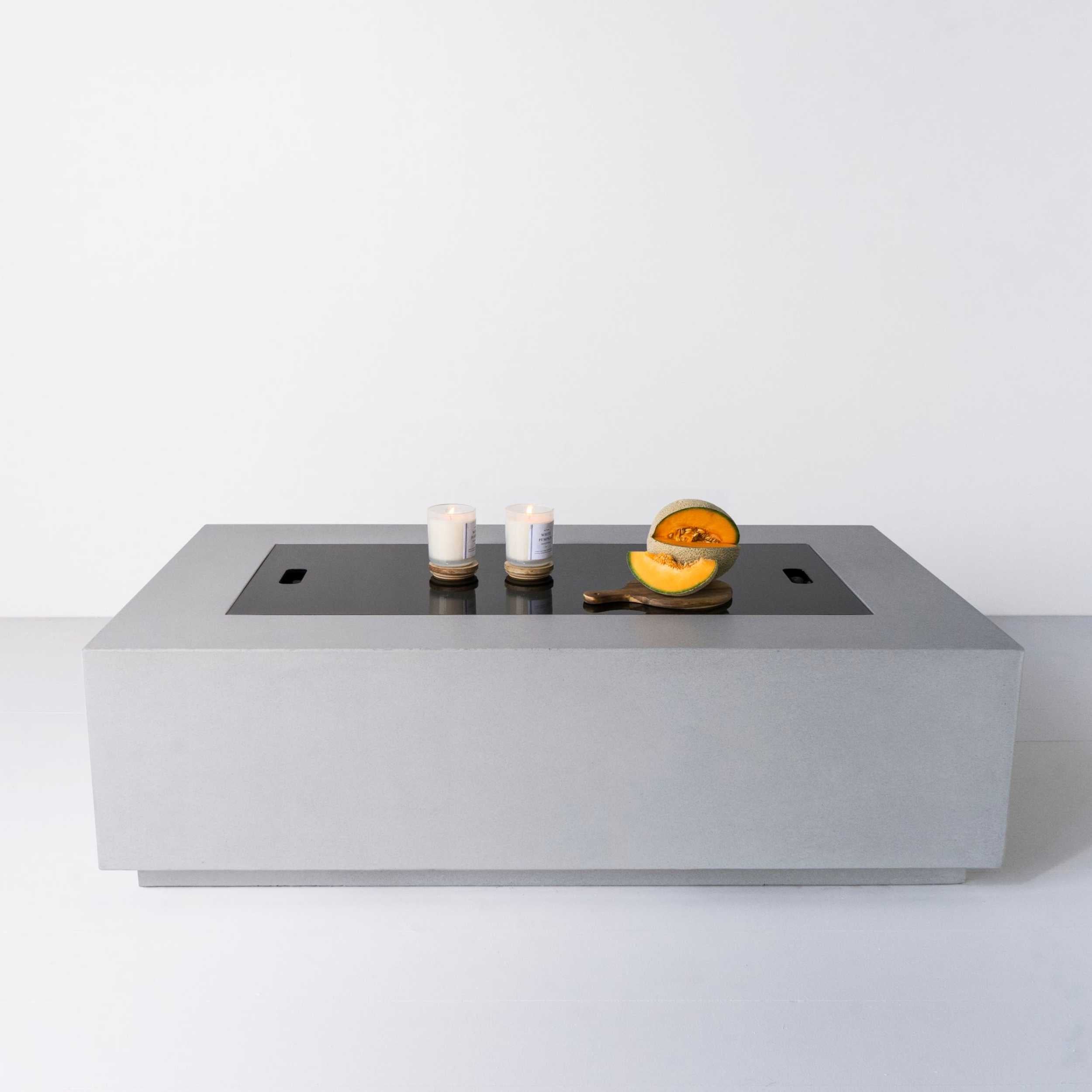 Lumera rectangular concrete firepit in light gray color with candle and cantelope on top of the fire pit cover - lifestyle shot