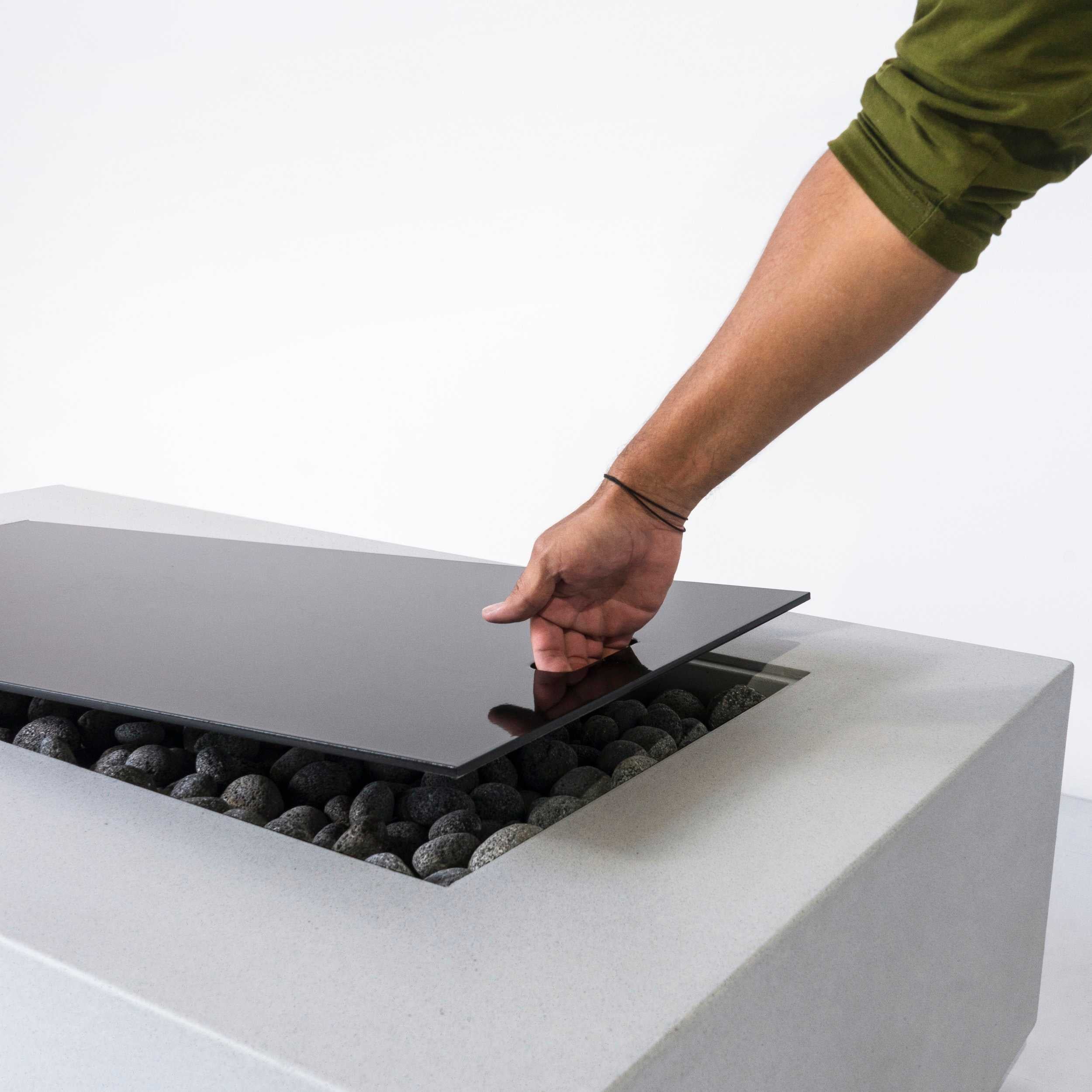 Close up of a man lifting the top cover off of the Lumera rectangular concrete firepit in light gray