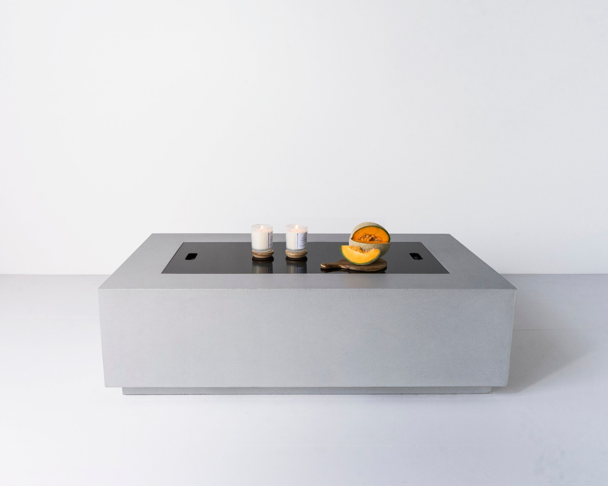 Lumera rectangular concrete firepit in light gray color with candle and cantelope on top of the fire pit cover - lifestyle shot