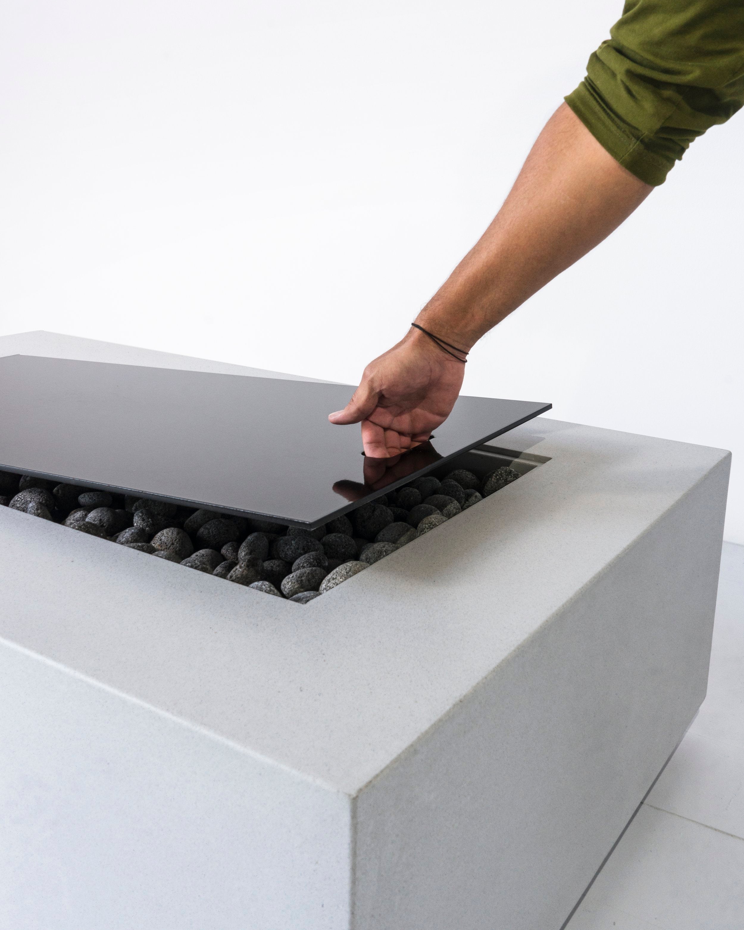 Close up of a man lifting the top cover off of the Lumera rectangular concrete firepit in light gray